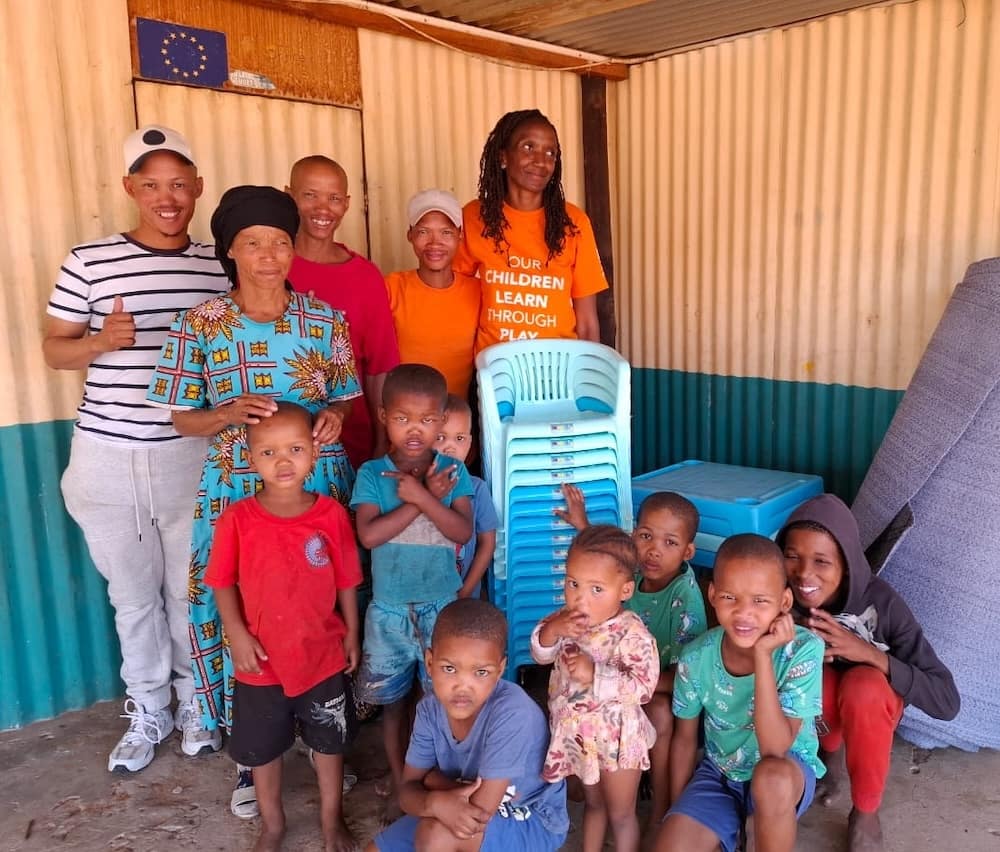 Smiling adults and children inside a tin walled building.