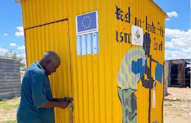A man unlocks a bright yellow free standing toilet door.